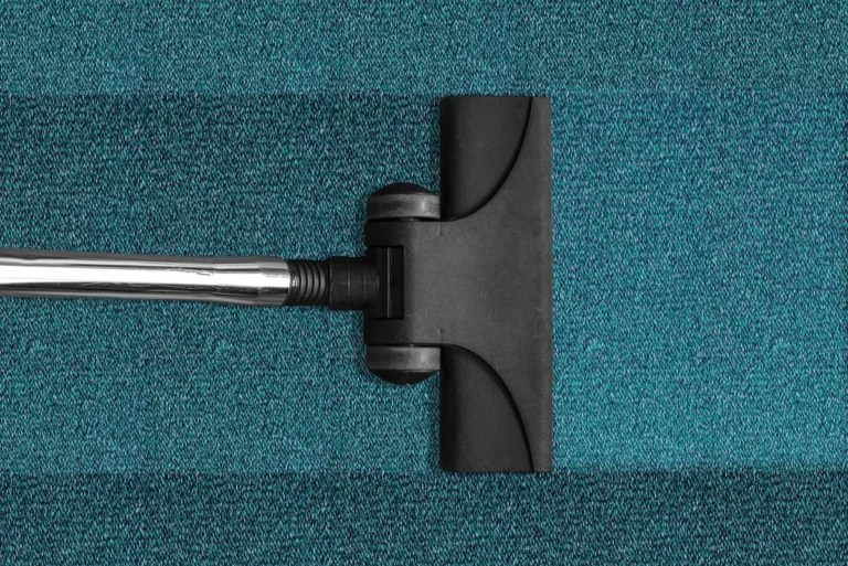 Green rug being cleaned by a vacuum.